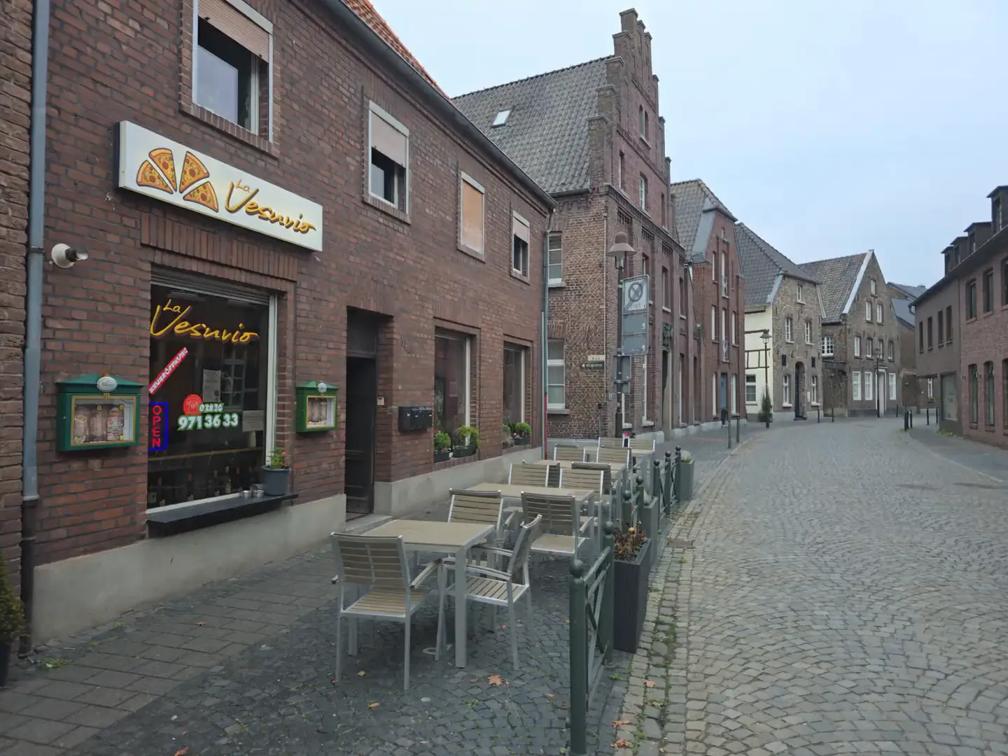 Die Pizzeria La Vesuvio in der Feldstraße in Wachtendonk: Backsteinhaus mit beleuchtetem Schild, Tische vor der Tür, Kopfsteinpflaster.