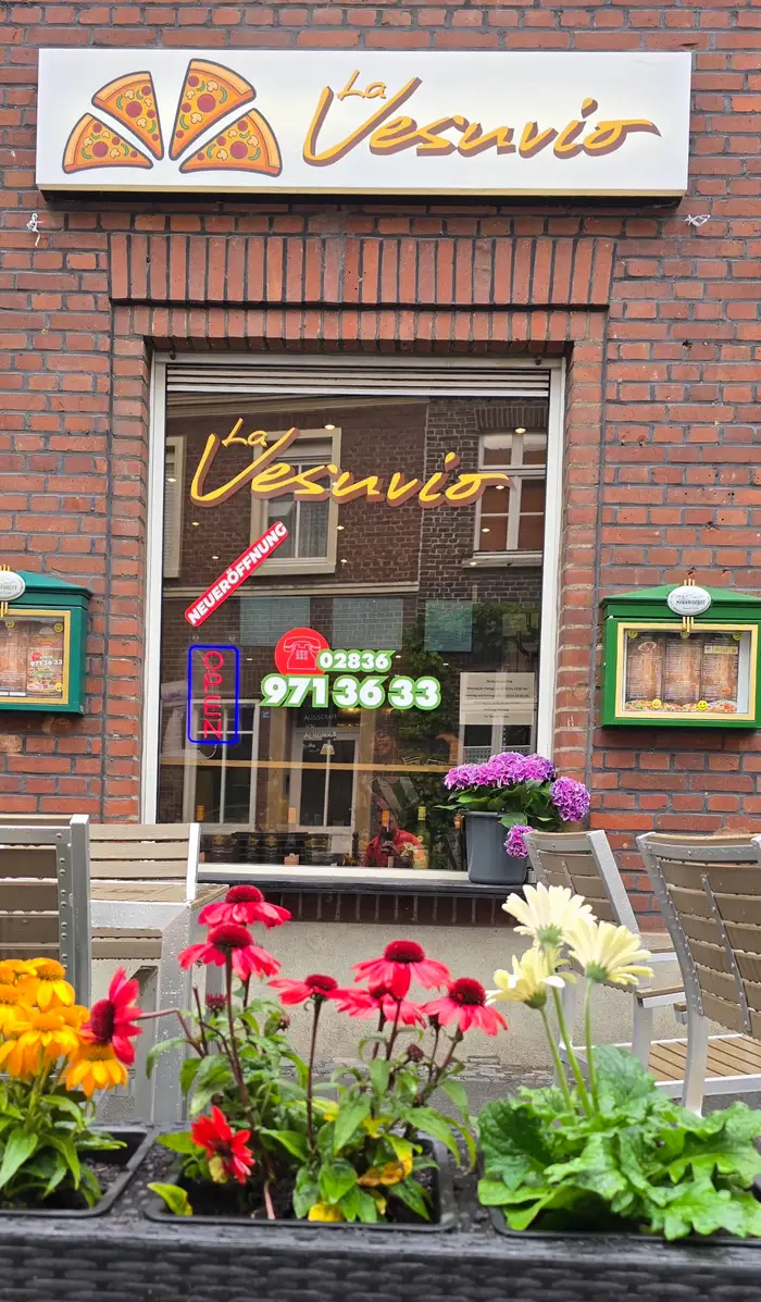 Das Schaufenster der Pizzeria La Vesuvio mit Schriftzug, Telefonnummer 02836 971 36 33 und Blumen vor der Tür.